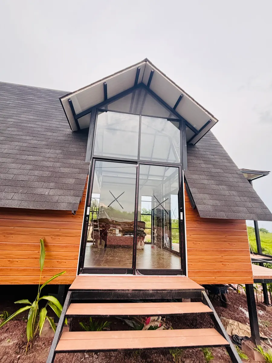 Fachada de cabaña con mampara y ventanal triangular de aluminio negro